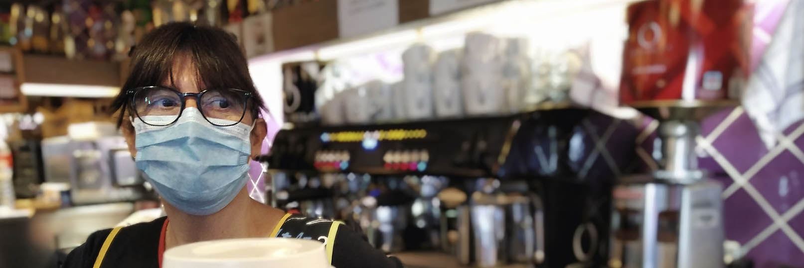 barista wearing a mask behind the counter of a cafe